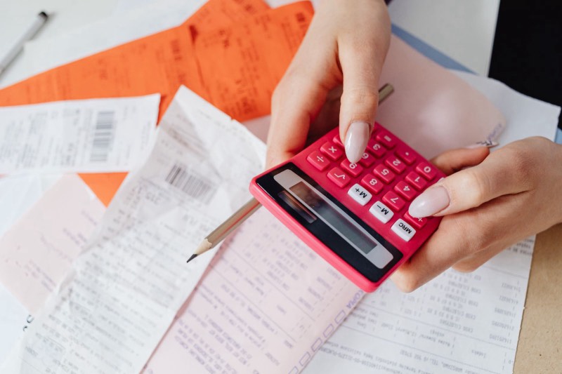 Une main calcule un budget avec une calculatrice parmi des factures