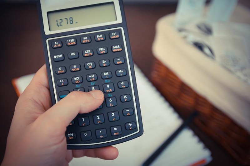 Une main tapote une calculatrice financière affichant un montant